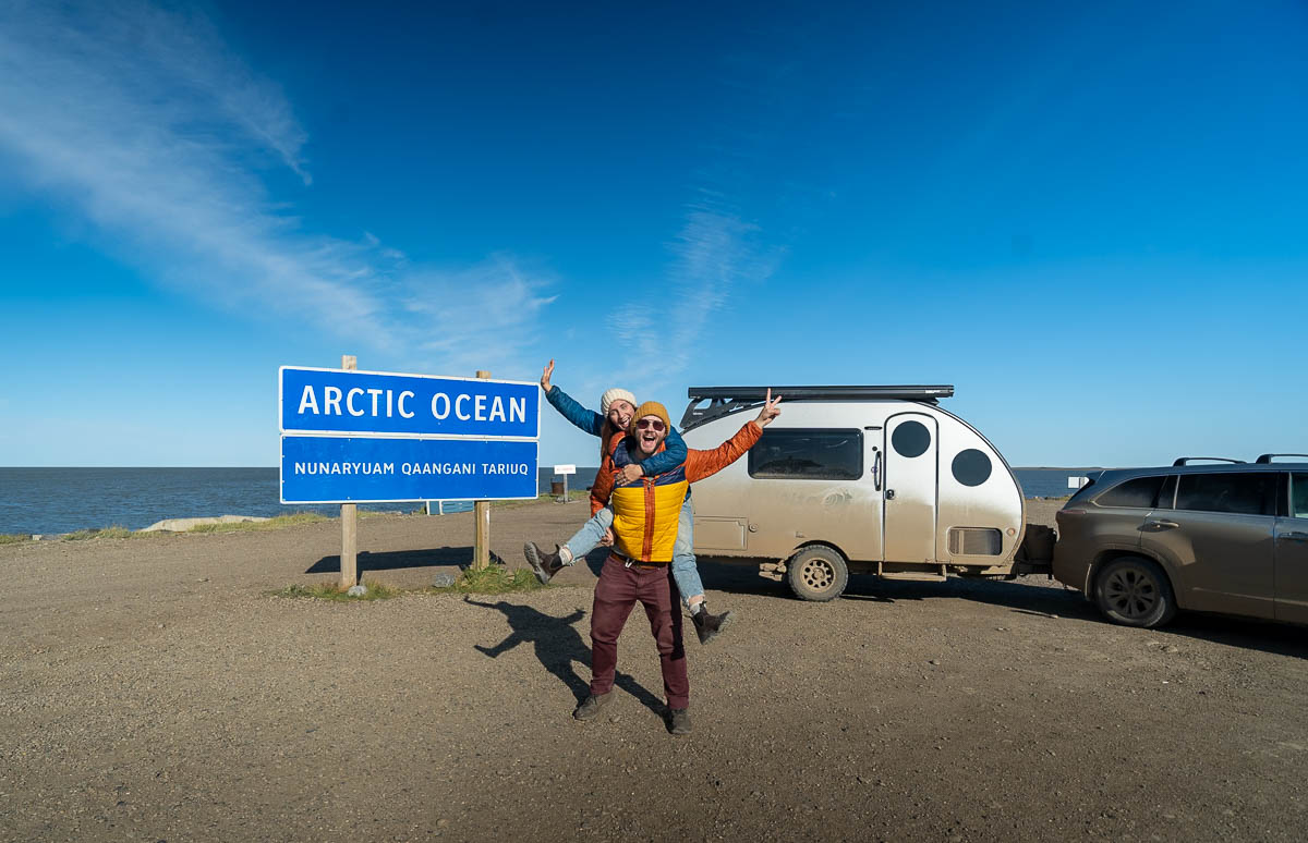 Couple standing in front of the Arctic Ocean sign in Tuktoyaktuk in the Northwest Territories of Canada 