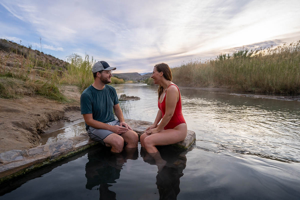 Couple sitting on the edge of Big Bend Hot Springs in the foundation of an old bathhouse along the Rio Grande River in Big Bend National Park in Texas