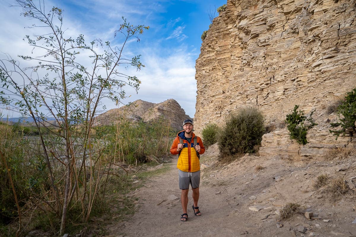 Man hiking along the Big Bend Hot Springs trail with limestone cliffs in the background in Big Bend National Park in Texas