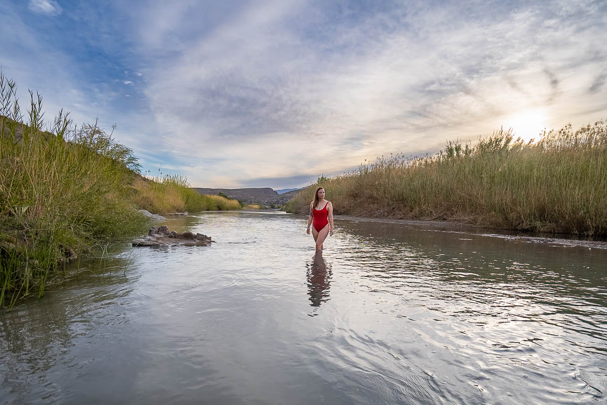 Woman in a swimsuit standing in the Rio Grande River with reeds and other marsh plants on the banks along the Big Bend Hot Springs trail in Big Bend National Park 