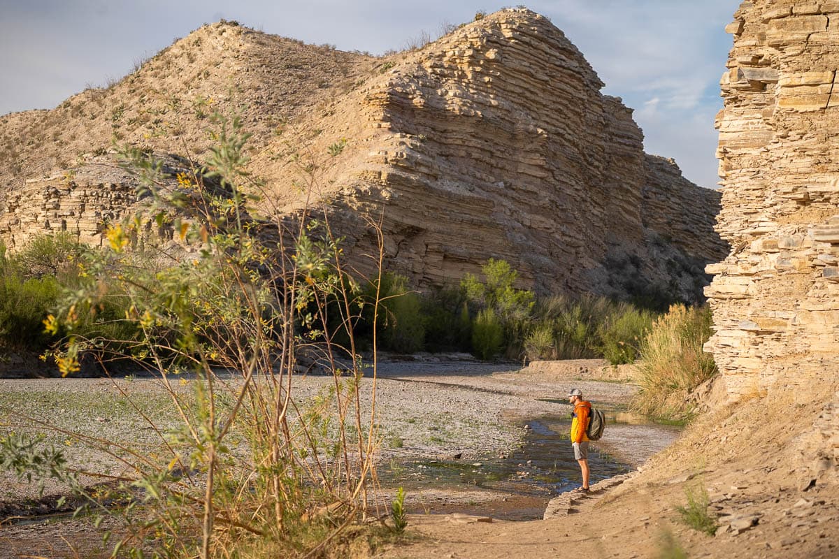 Man standing along the banks of the Rio Grande with a limestone cliff in the background along the Langford Hot Springs trail in Big Bed National Park in Texas