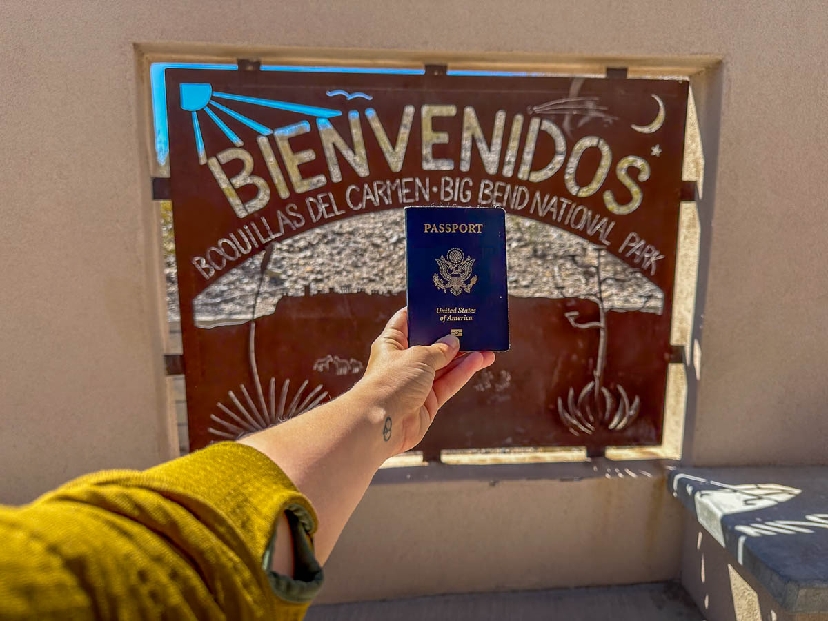 Hand holding passport in front of sign for Boquillas del Carmen at the Boquillas Crossing in Big Bend National Park