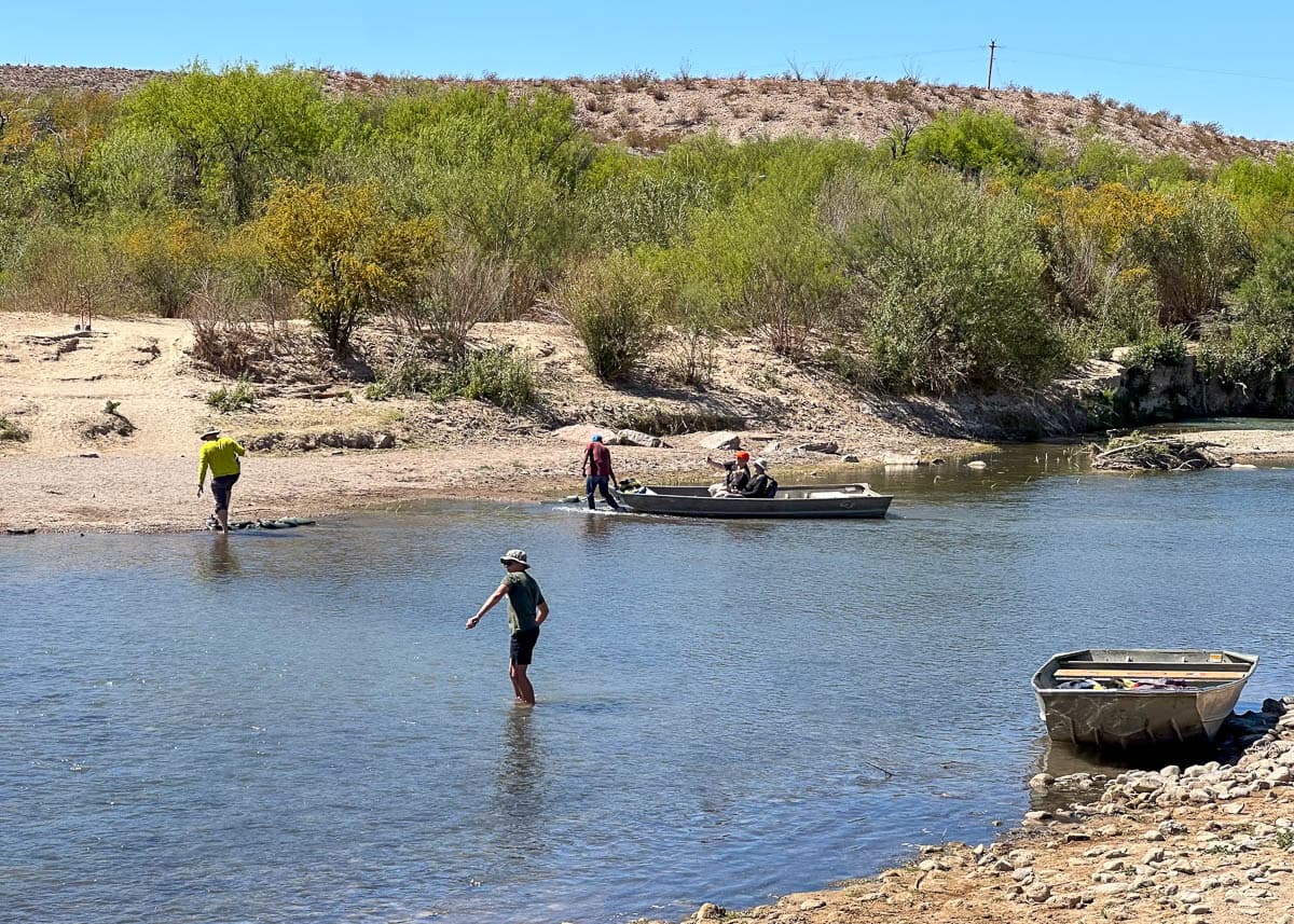 Man pulling a rowboat and visitors walking across the Rio Grande in between Boquillas del Carmen and Big Bend National Park