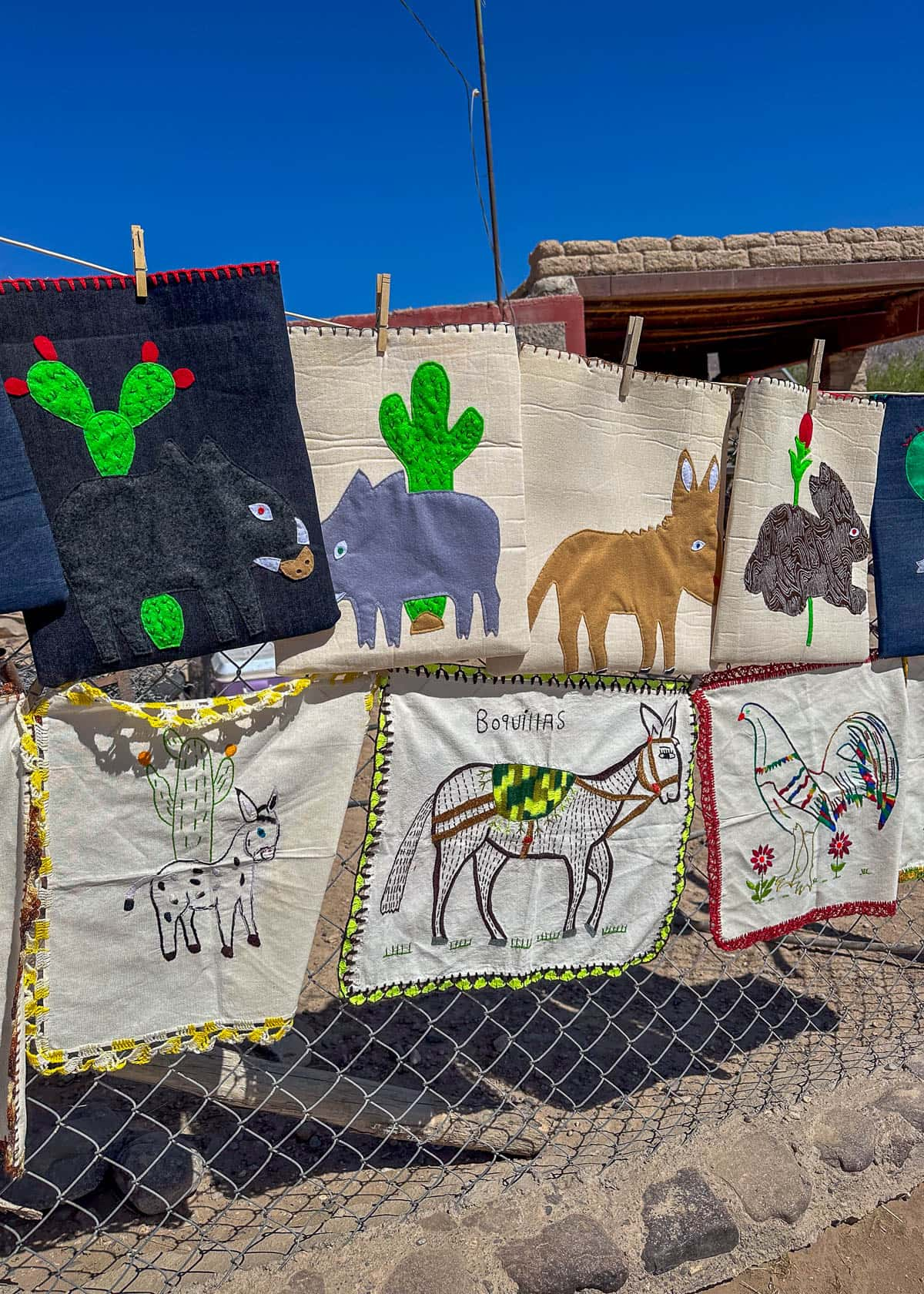 Embroidered bags and towels hanging from a chain link fence being sold by vendors at Boquillas del Carmen, Mexico