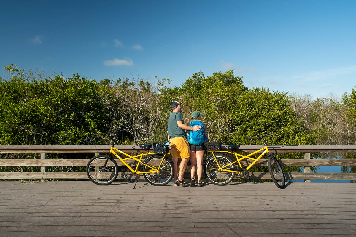 Couple standing with yellow bikes along a wooden boardwalk along the Shark Valley bike trail in Everglades National Park