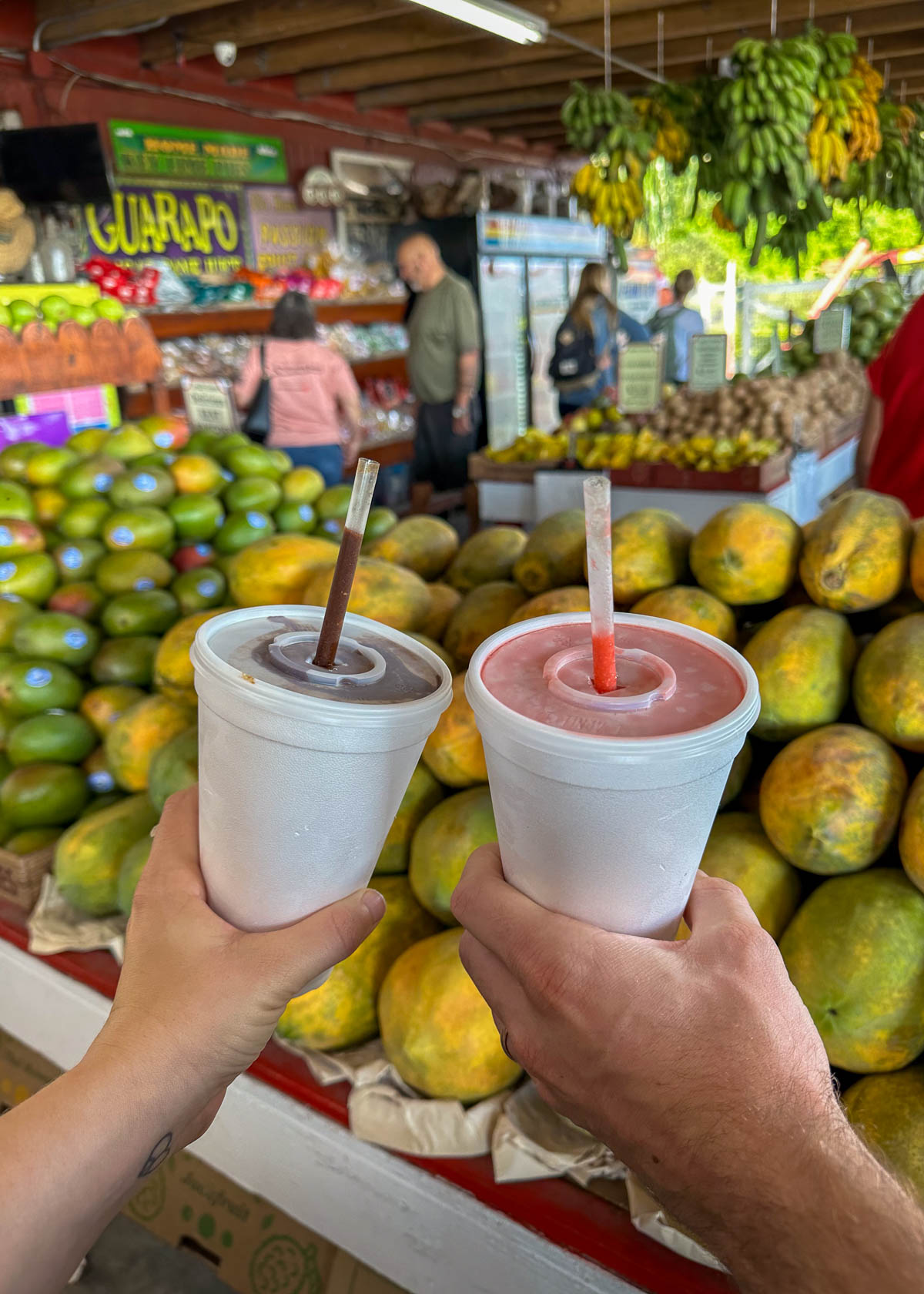 Couple holding smoothie cups in front of fruit stands at Robert is Here fruit stand in Homestead, Florida