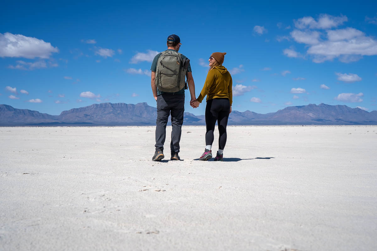 Couple holding hands on the Alkali Flat with San Andres Mountains in the background along the Alkali Flat Trail in White Sands National Park