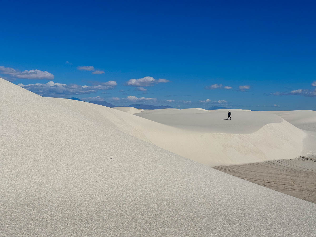 Man walking on white sand dunes along the Alkali Flat Trail in White Sands National Park in New Mexico