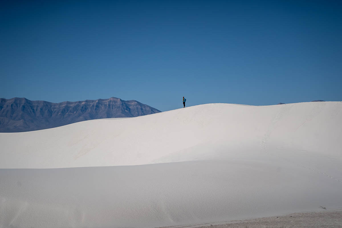 Woman walking on a white sand dune with the San Andres Mountains in the background along the Alkali Flat Trail in White Sands National Park in New Mexico