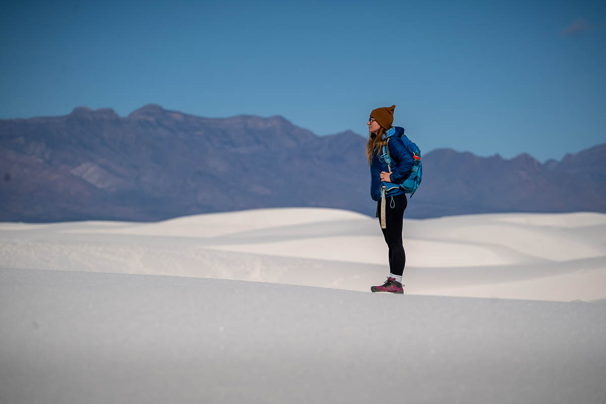 Woman standing on sand dunes with San Andres Mountains along the Alkali Flat Trail in White Sand National Park in New Mexico