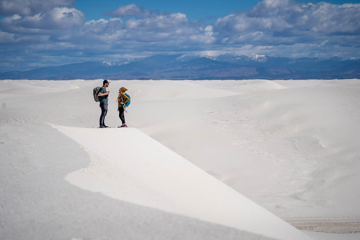 Couple smiling on top of a white sand dune along the Alkali Flat Trail with mountains in the background along the White Sands National Park in New Mexico