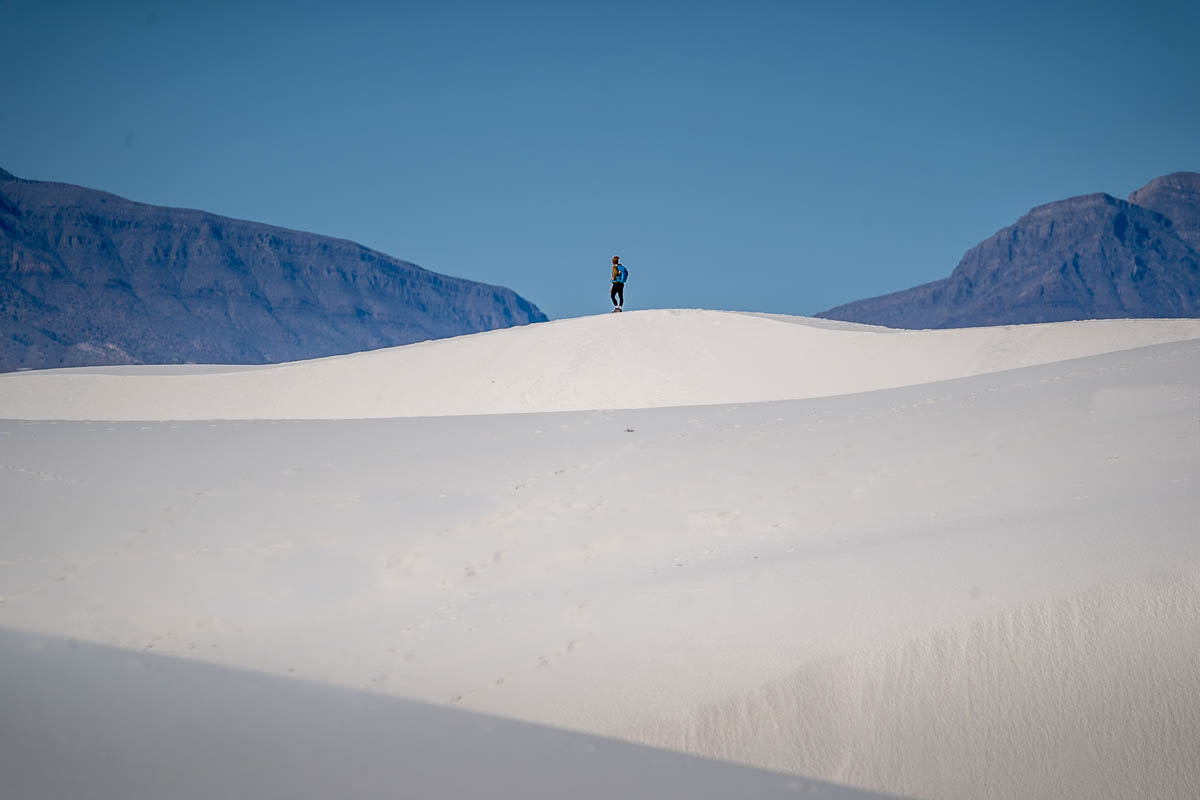 Woman standing on a sand dune with mountains in the background along the Alkali Flat Trail in White Sands National Park in New Mexico