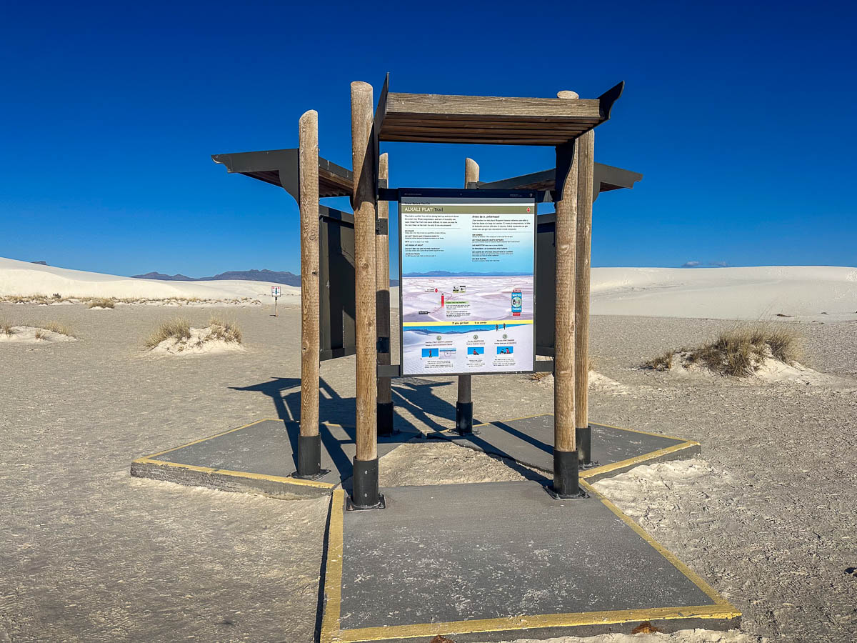 Trailhead sign for Alkali Flat Trail with white sand dunes in the background in White Sands National Park in New Mexico