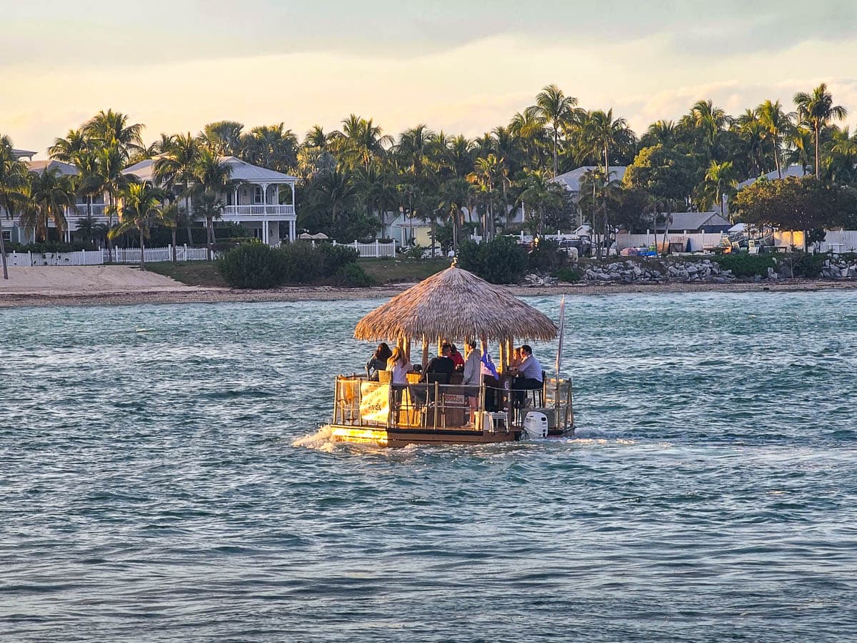 People cruising on a tiki boat with plantation homes and palm trees in the background in Key West, Florida