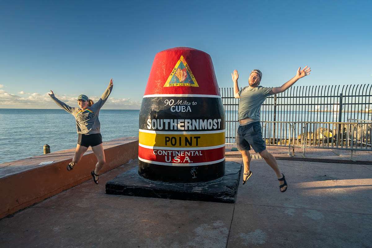 Couple jumping near the Southernmost point marker in Key West, Florida