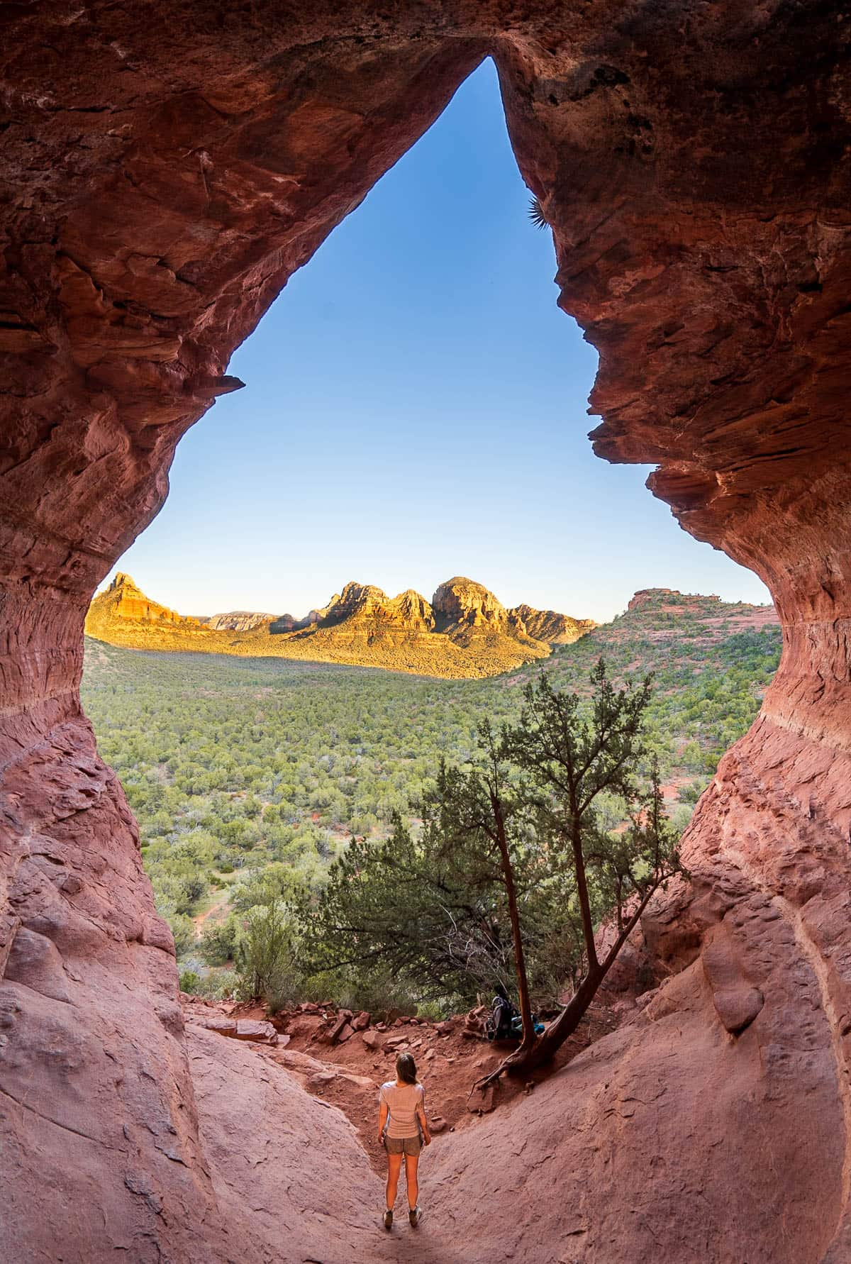 Woman standing at the base of the Birthing Cave, overlooking the surrounding red rock mesas in Sedona, Arizona