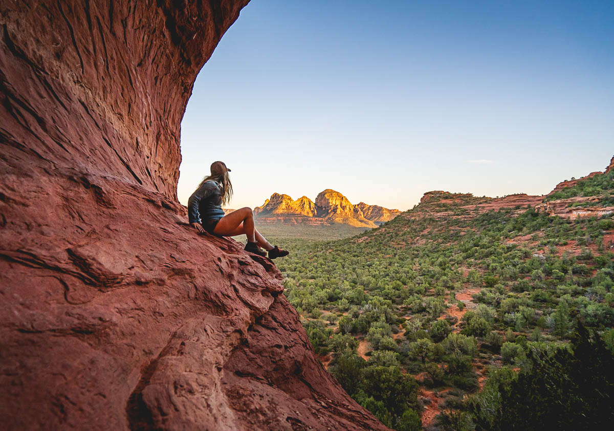 Woman sitting on a curved stone wall, overlooking the surrounding red rock mesas, in the Birthing Cave in Sedona, Arizona