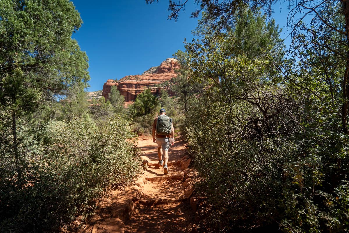 Man hiking along the Boynton Canyon trail with red rock formation in the background in Sedona, Arizona