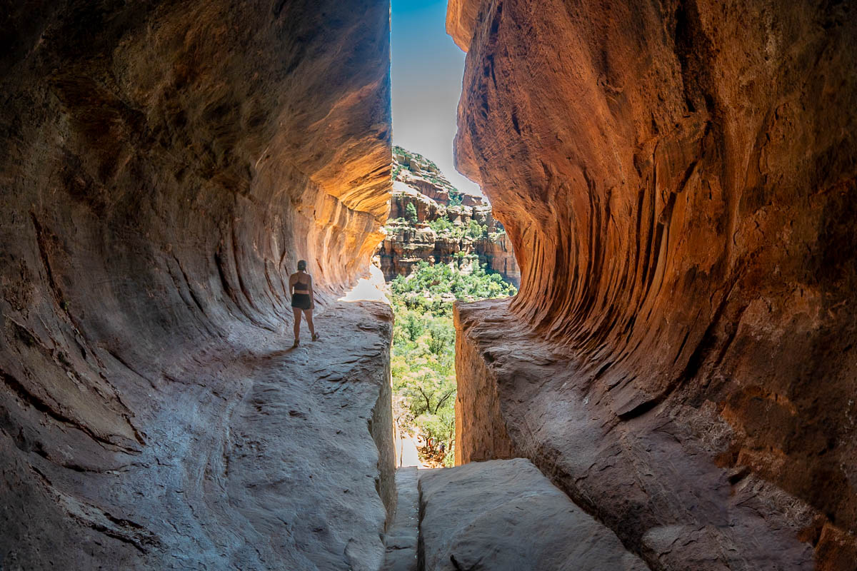 Woman walking along a ledge in the Subway Cave with red rock formation in the background in Sedona, Arizona