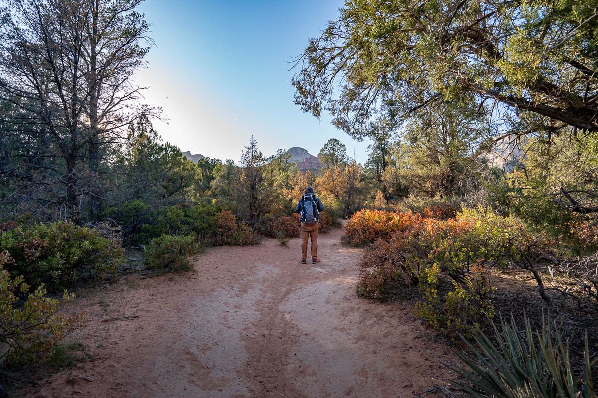 Man hiking along the Birthing Cave Trail with red rock formation in the background in Sedona, Arizona