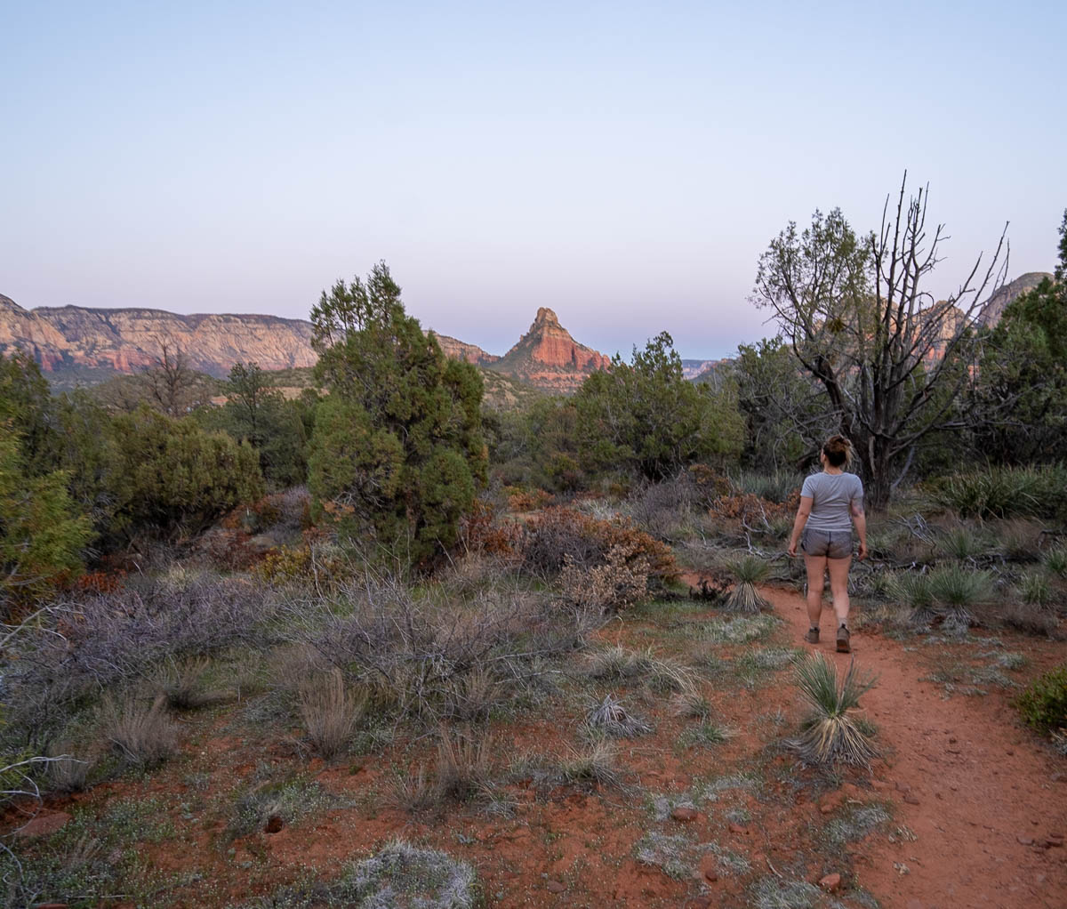 Woman walking on the Birthing Cave Trail with red rock formation in the background in Sedona, Arizona