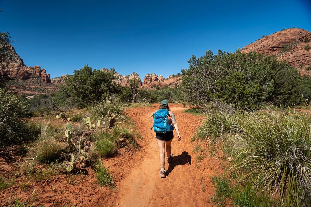 Woman hiking along the Keyhole Cave Trail with red rock formations in the background of Sedona, Arizona