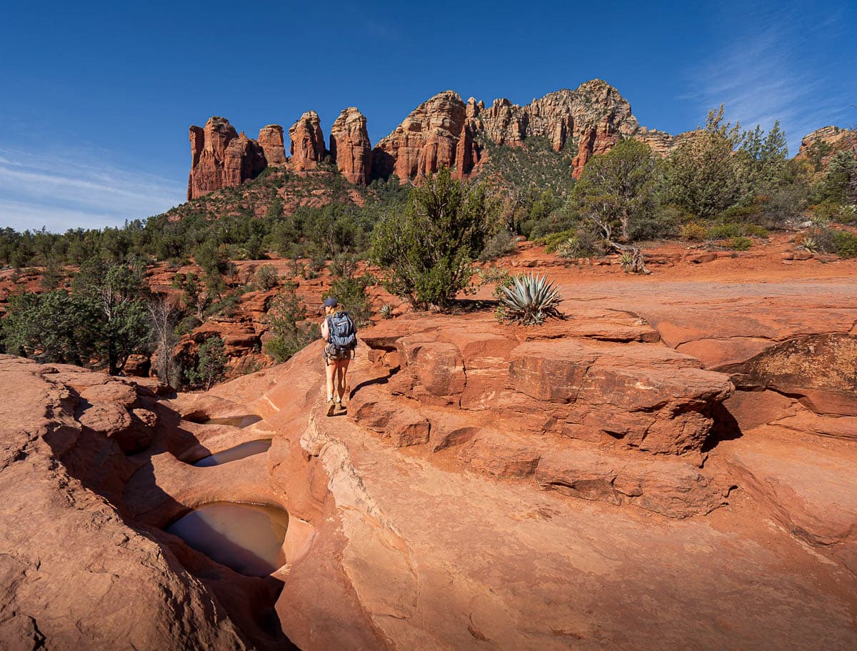 Woman hiking along the Seven Sacred Pools with rock formations in the background along the Soldier Pass Trail in Sedona, Arizona