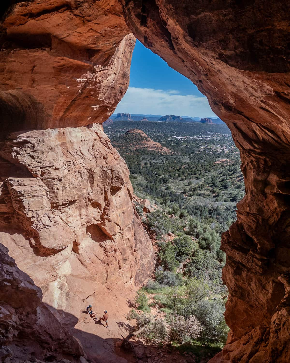 Couple standing in the opening of the Keyhole Cave with rock formations in the background in Sedona, Arizona