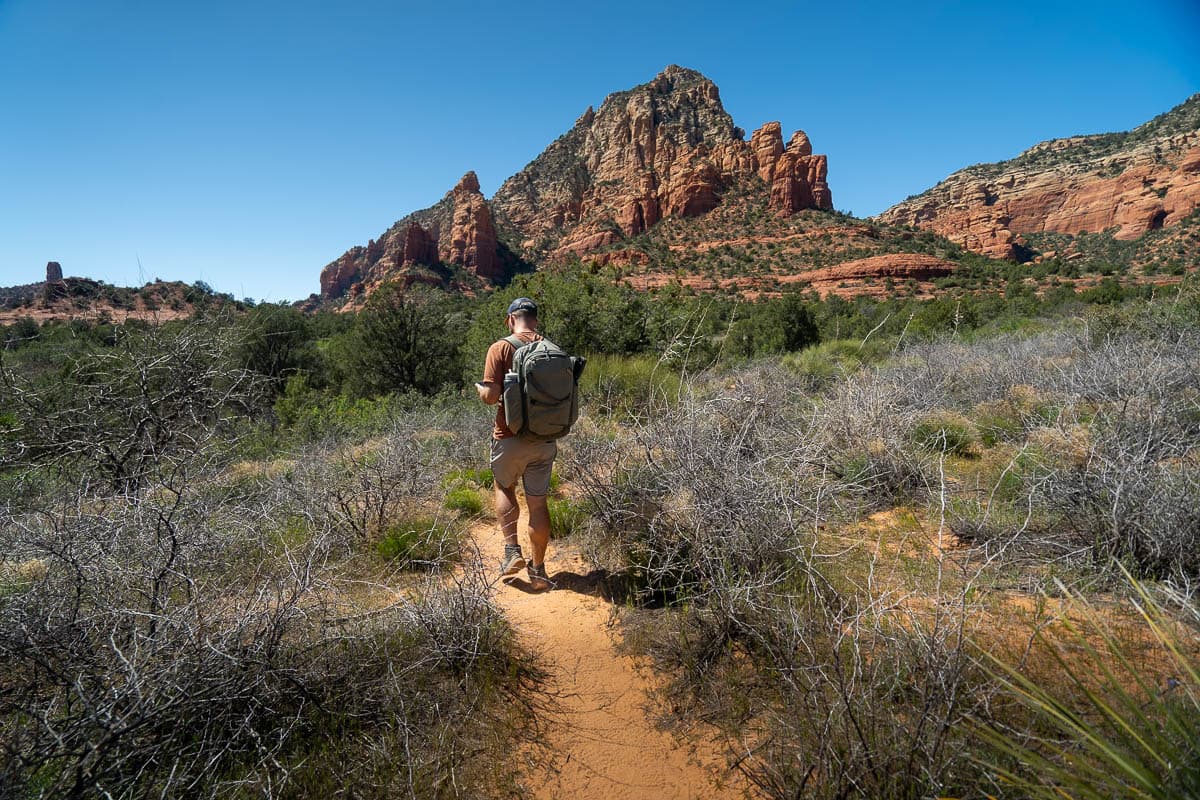 Man hiking along the Keyhole Cave Trail with red rock formations in the background of Sedona, Arizona