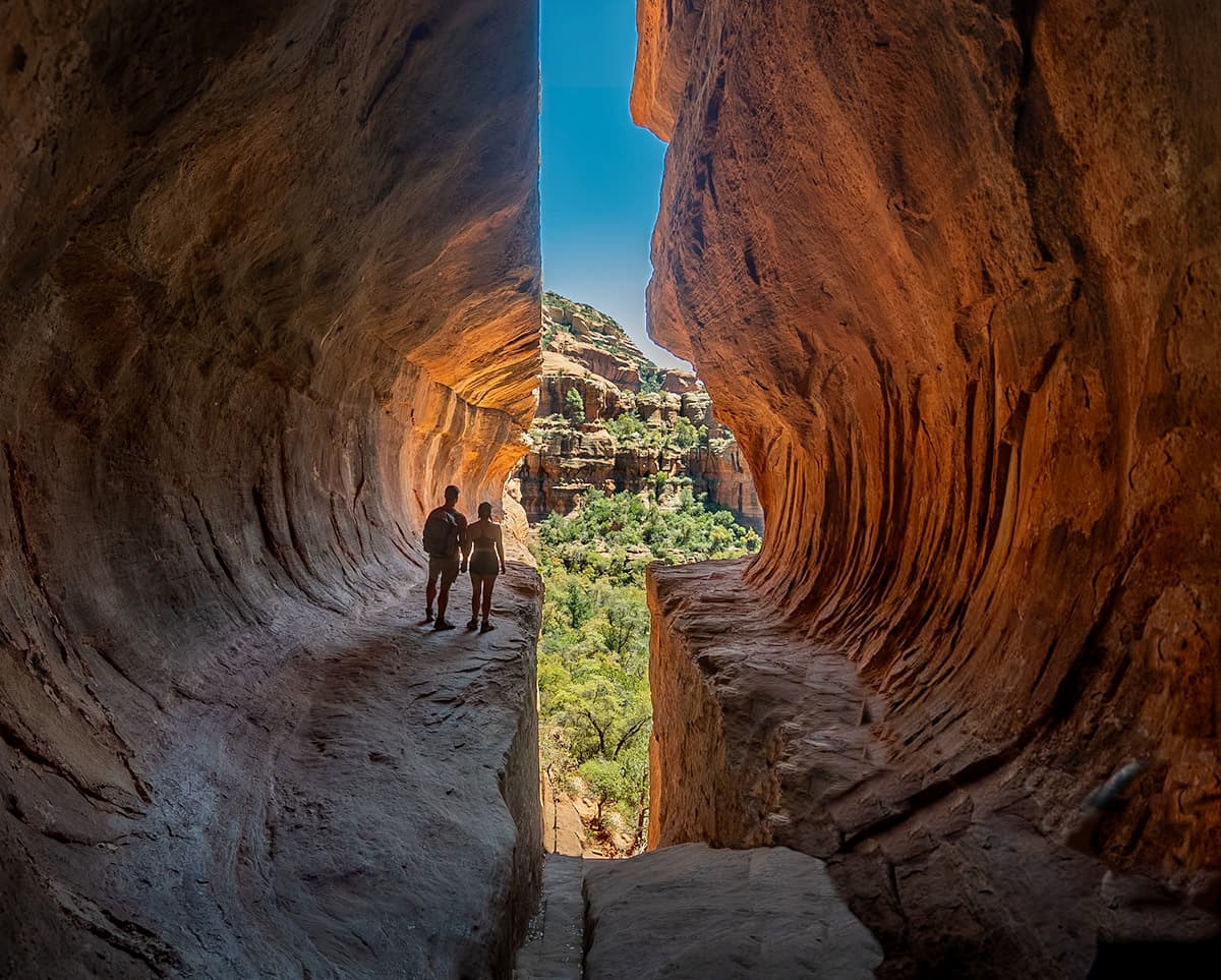 Couple holding hands on a ledge with a red rock formation in the background in the Subway Cave in Sedona, Arizona