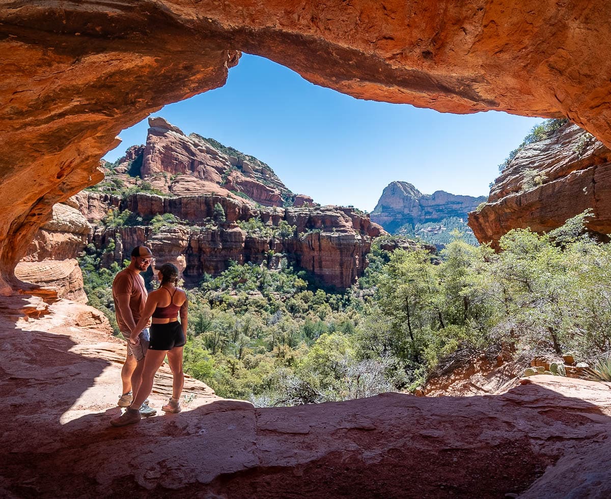 Couple standing along the ledge of the Subway Cave with rock formations in the background in Sedona, Arizona