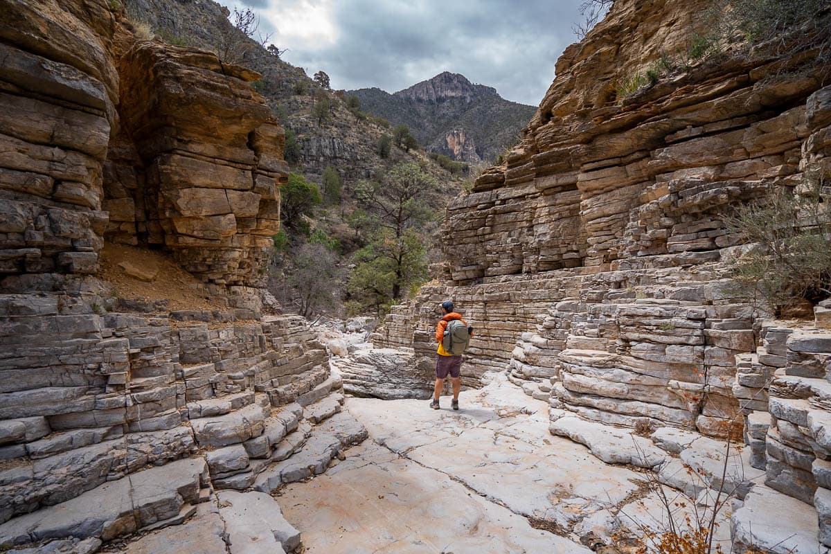 Man standing between a cliff of rocky layers along the Devil's Hall Trail in Guadalupe Mountains National Park