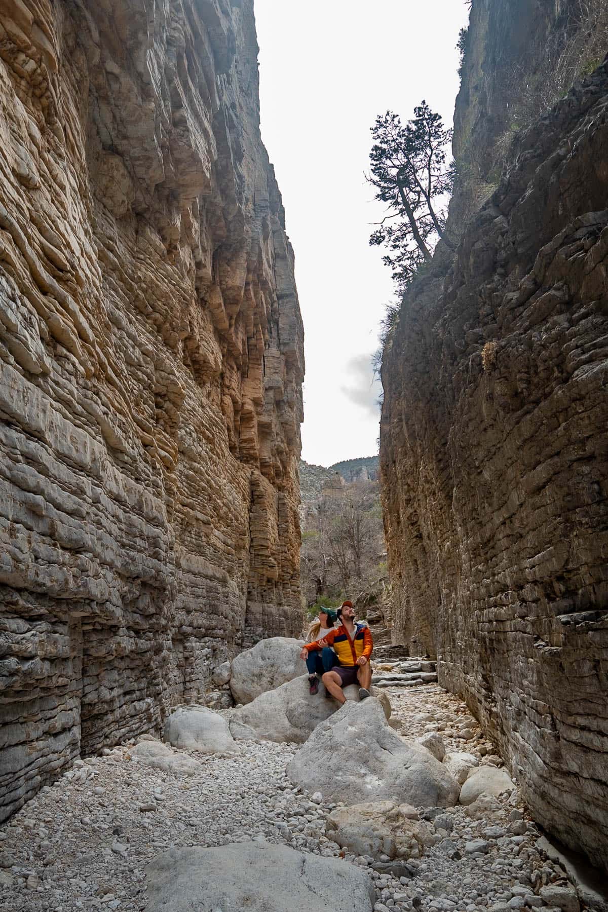 Couple sitting on a boulder between the Devil's Hall slot canyon along the Devil's Hall Trail in Guadalupe Mountains National Park in Texas