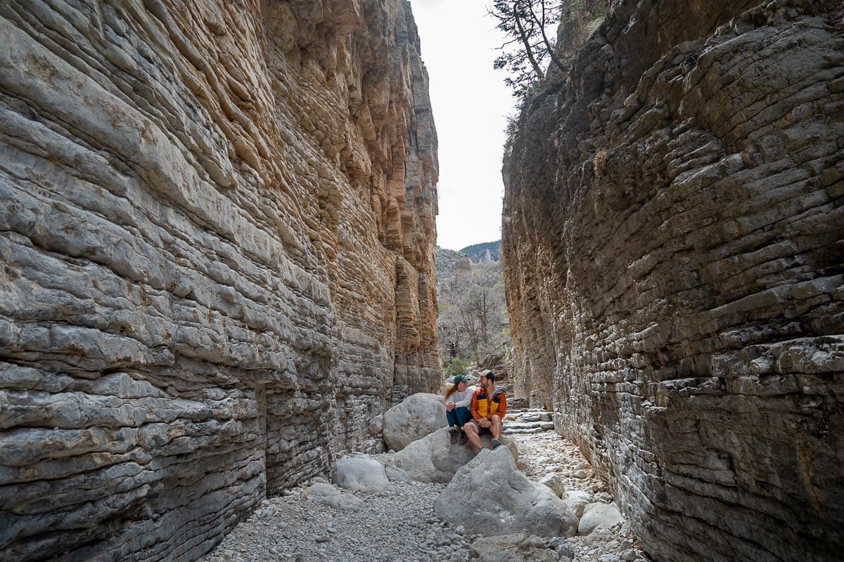 Couple looking at each other on a boulder in the Devil's Hall slot canyon along the Devil's Hall Trail in Guadalupe Mountains National Park in Texas