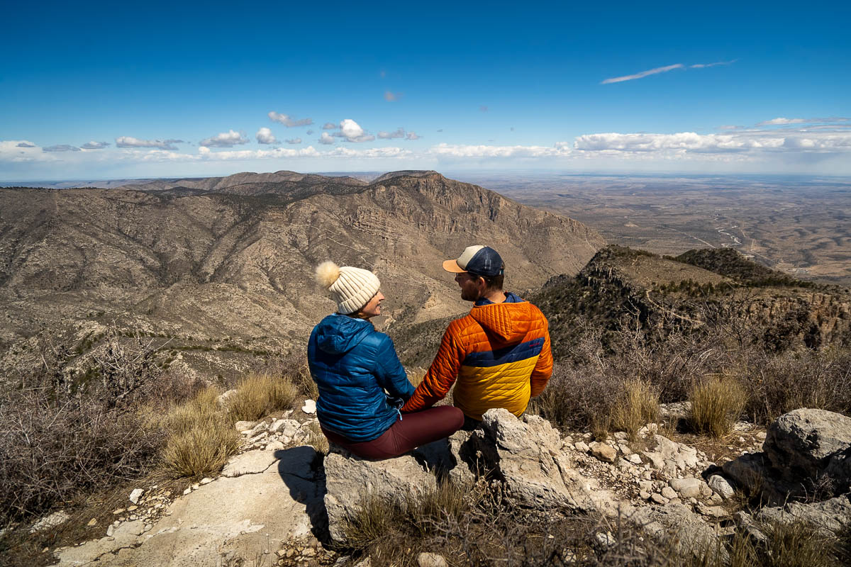 Couple sitting at the summit of Guadalupe Peak with Hunter Peak in the background in Guadalupe Mountains National Park in Texas