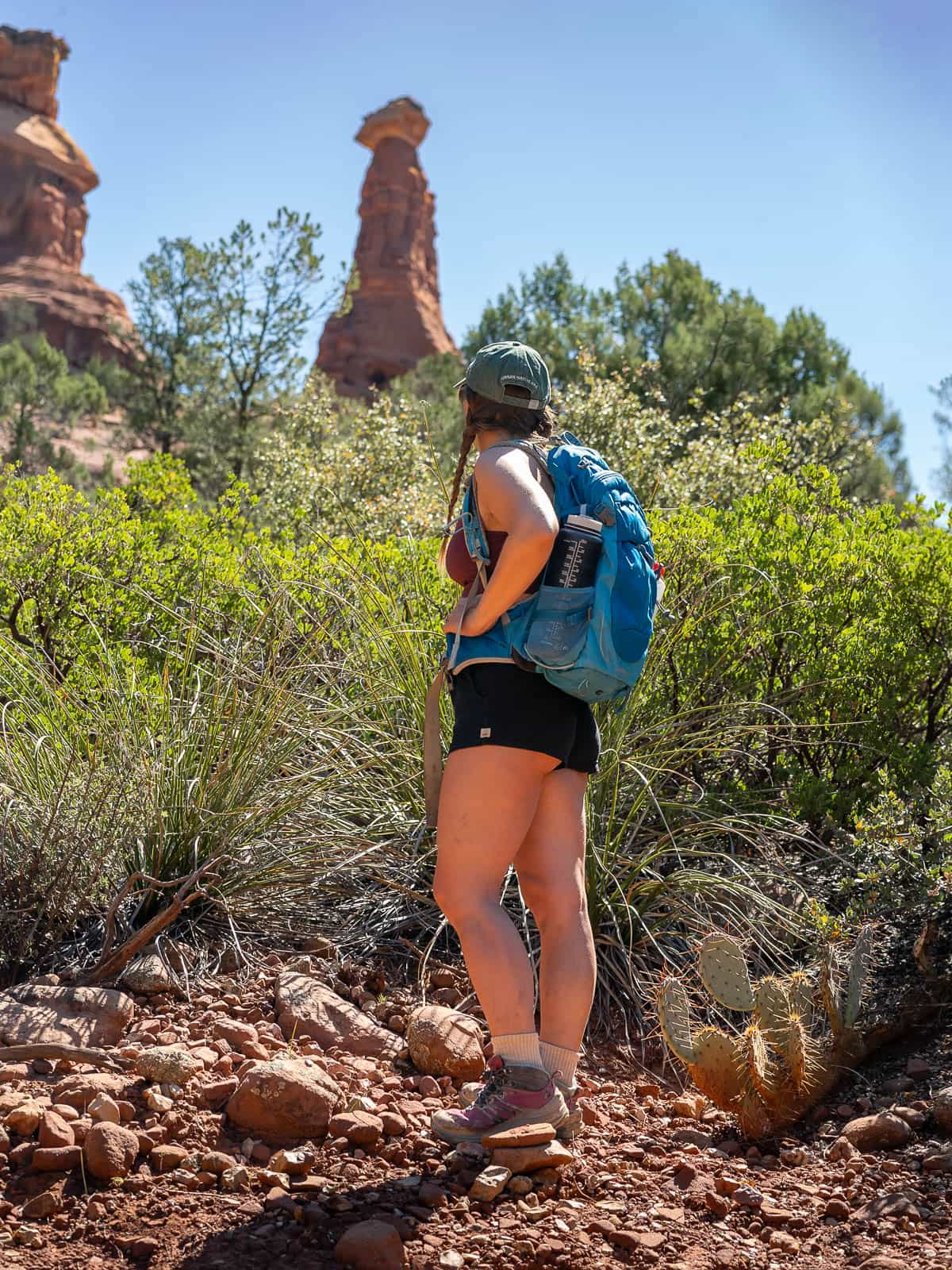 Woman looking at the Boynton Vista vortex with greenery in the background along the Boynton Canyon Trail in Sedona, Arizona