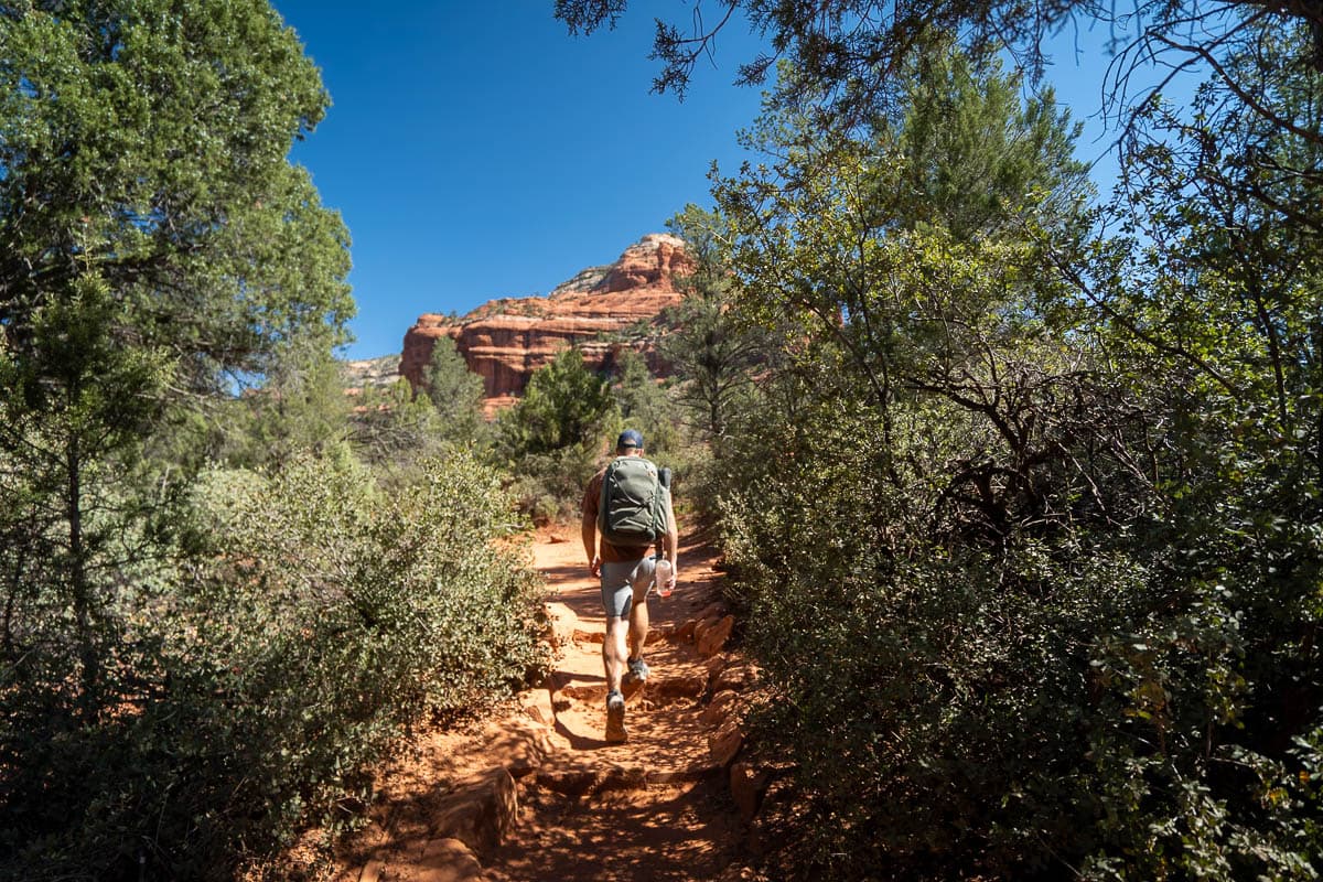 Man hiking along the Boynton Canyon Trail with a rock formation the background in Sedona, Arizona