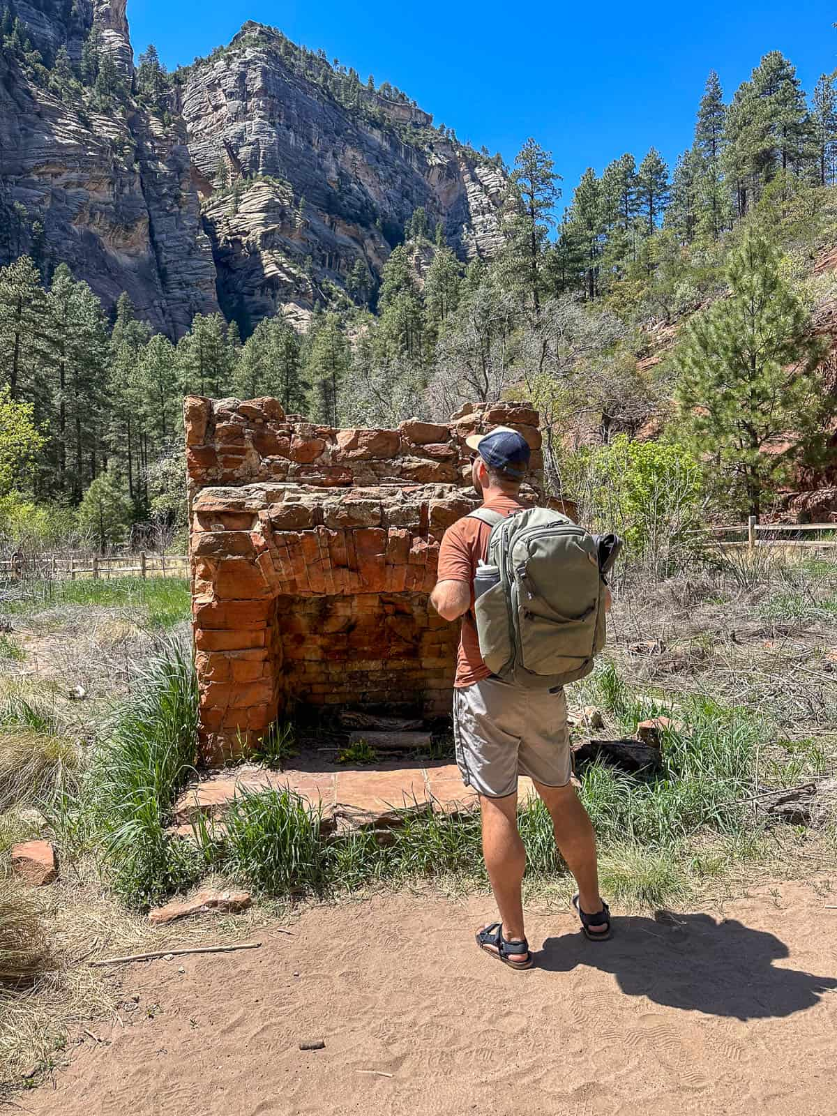 Man standing in front of rock chimney  at the Mayhew Lodge ruins along the West Fork Trail in Sedona, Arizona