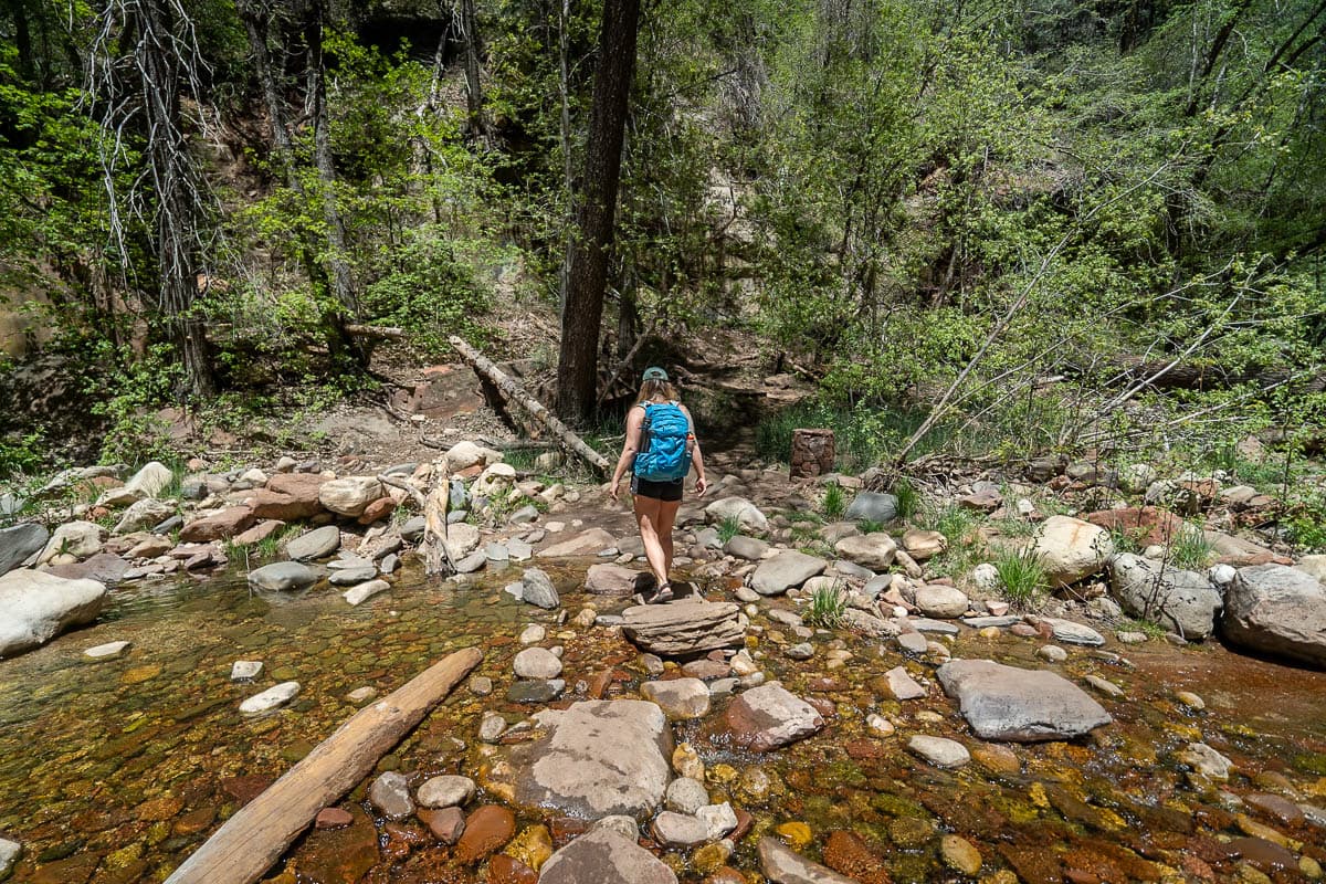 Woman hiking across the rocks of Oak Creek along the West Fork Trail in Sedona, Arizona