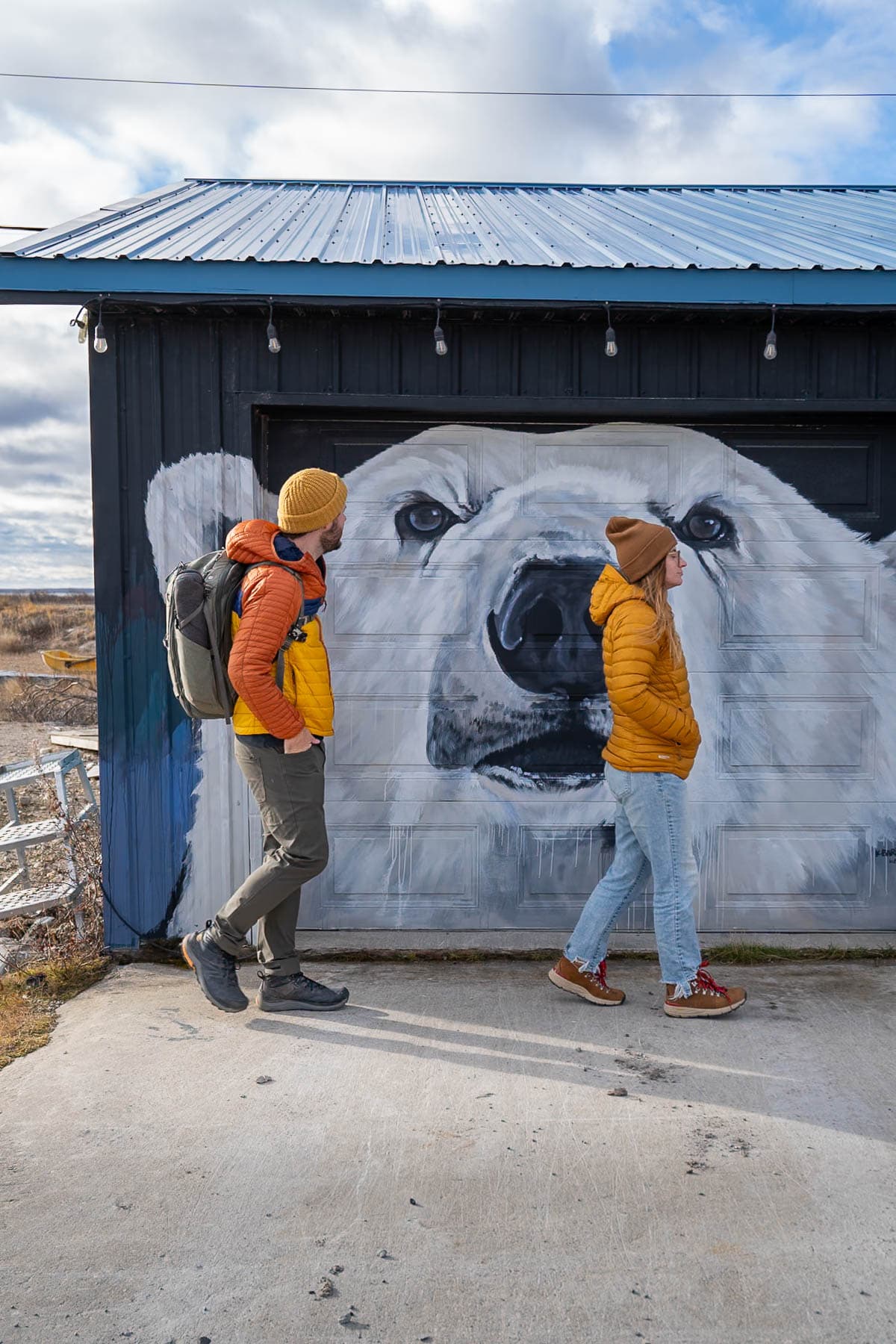 Couple walking in front of polar bear mural painted on a garage in Churchill, Manitoba