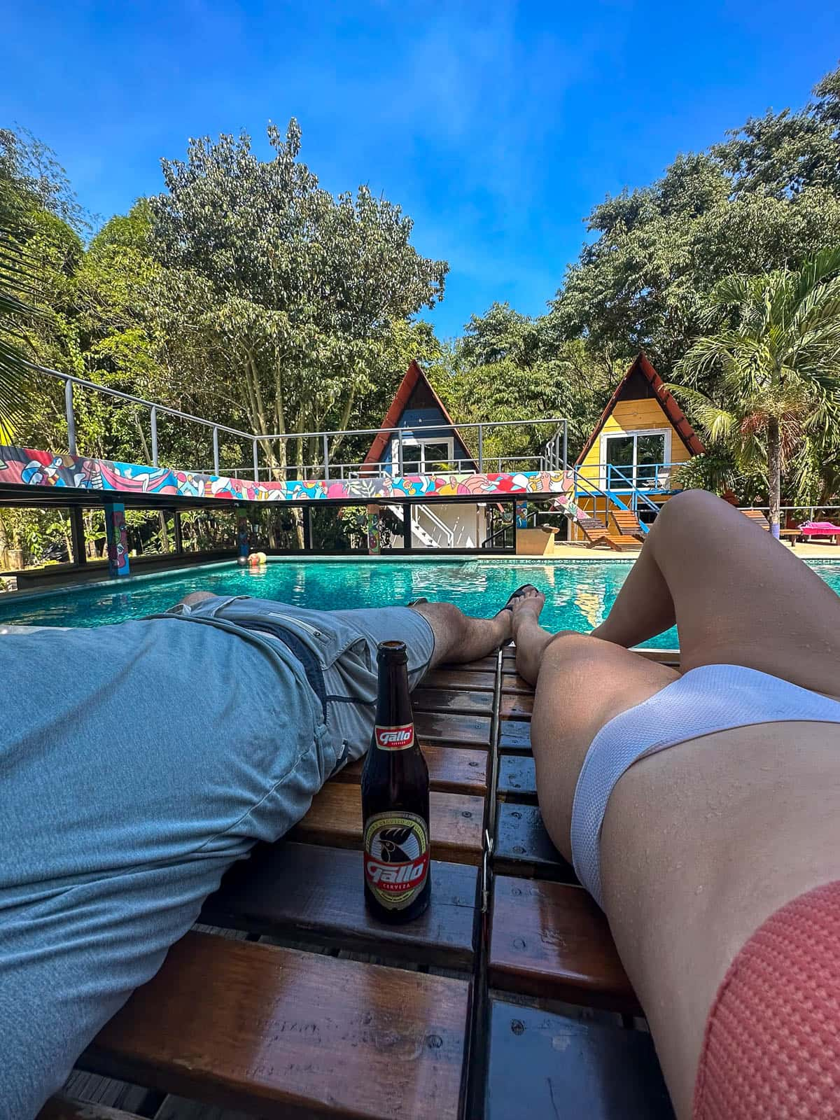 Couple laying by a pool in front of A-frame cabins in Greengo's Hotel in Lanquin, Guatemala