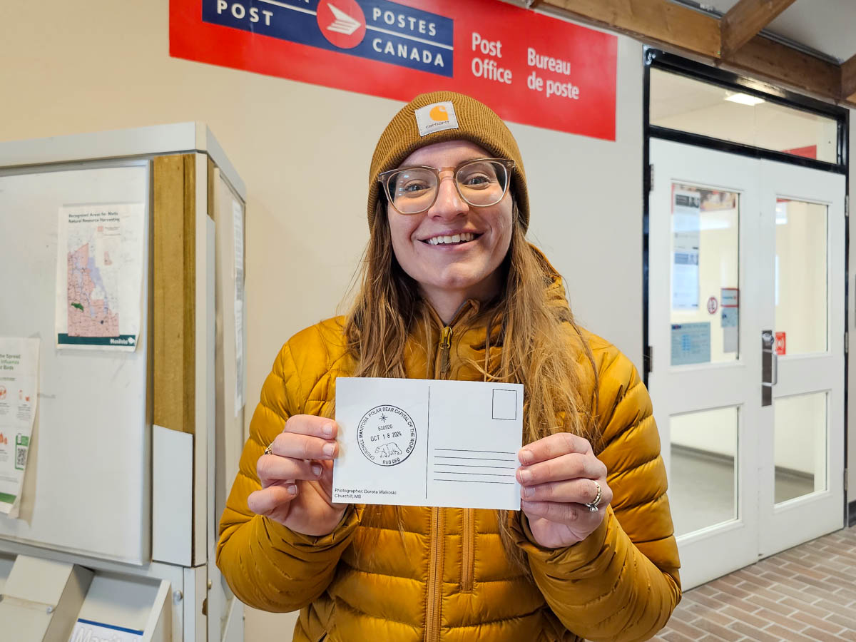 Woman holding a postcard with a polar bear passport stamp in Churchill, Manitoba