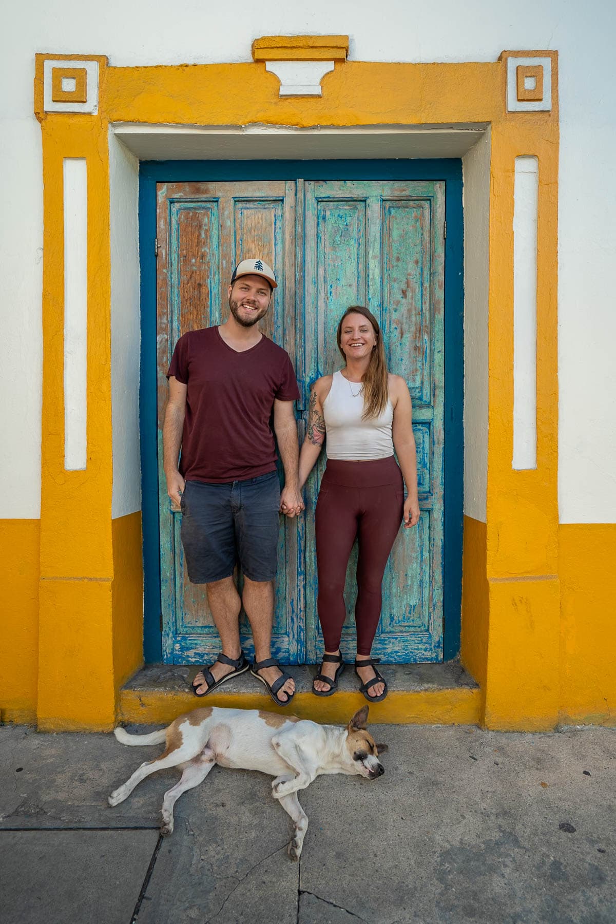 Couple holding hands with a dog at their feet with a colorful building in the background in Flores, Guatemala