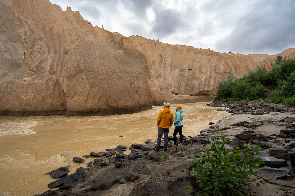 Couple standing along the Ukak River, looking at a wall made of ash, in the Valley of Ten Thousand Smokes in Katmai National Park in Alaska