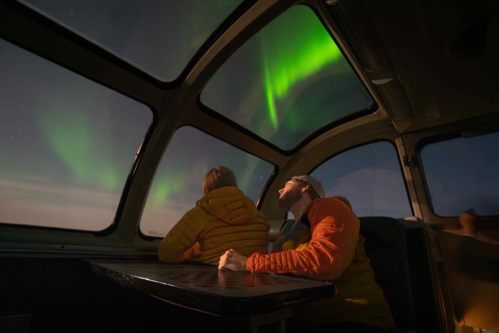 Couple sitting on the dome car of the Via Rail train to Churchill, Manitoba, looking at the Northern Lights