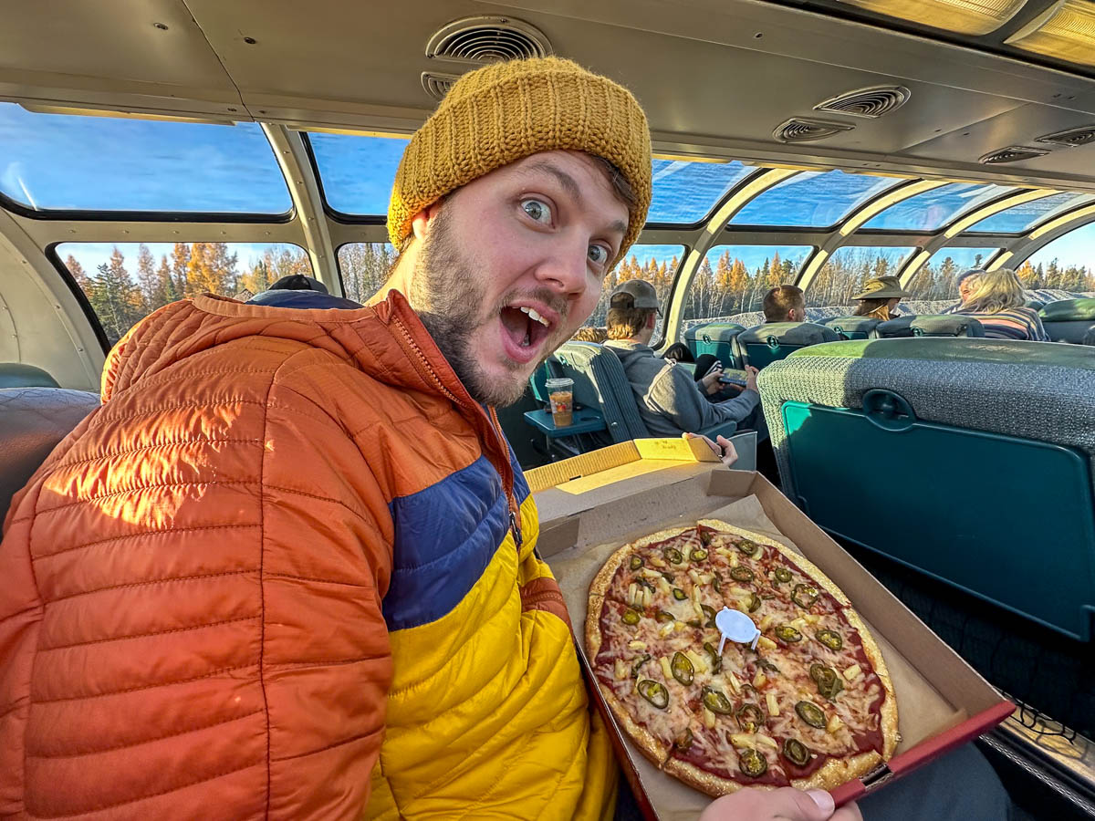 Man holding a pizza on the Skyline Dome train to Churchill, Manitoba