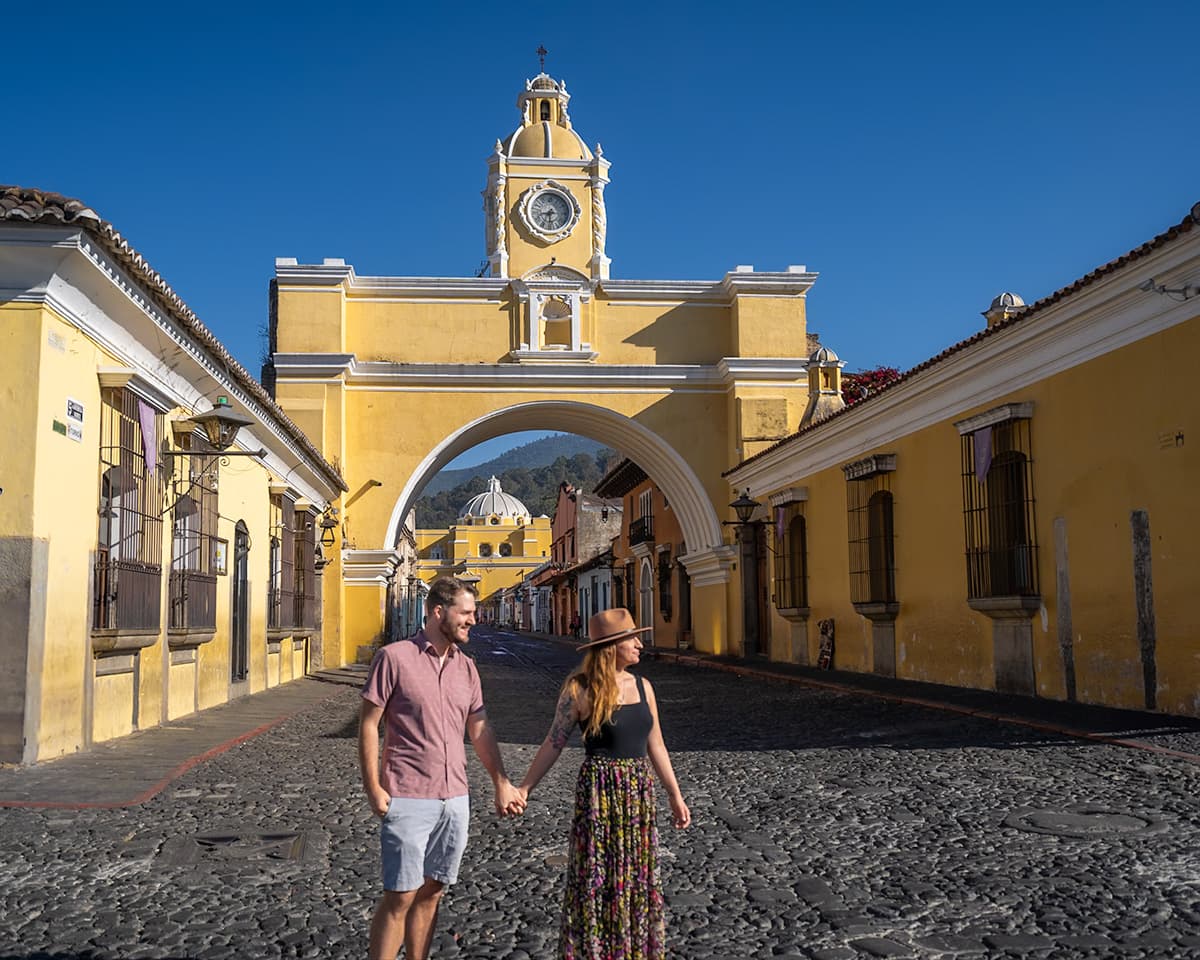 Couple holding hands and walking in front of the Arco de Santa Catalina in Antigua, Guatemala