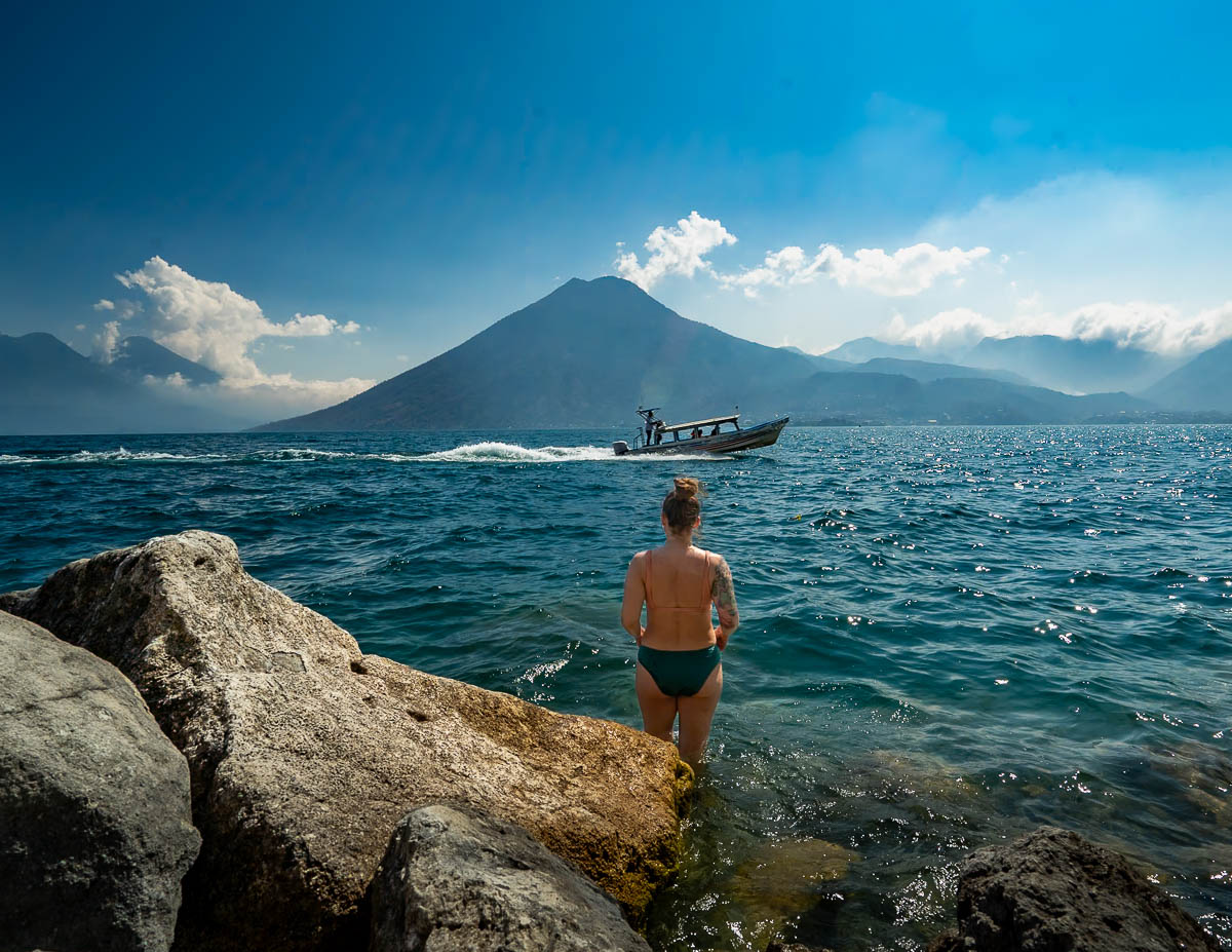 Woman standing in Lake Atitlan and watching a lancha drive past the San Pedro Volcano in the background in Guatemala