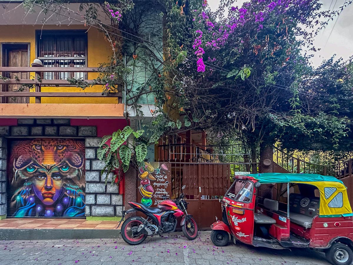 Colorful mural on a building with a tuk tuk and motorcycle parked on a street in San Pedro in Lake Atitlan, Guatemala