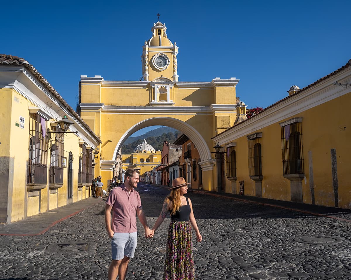 Couple holding hands and walking in front of the Santa Catalina Arch in Antigua, Guatemala